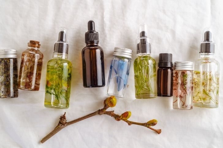 Transparent bottles or essential oil with fresh herbs and flowers, natural teartment for health and beauty.