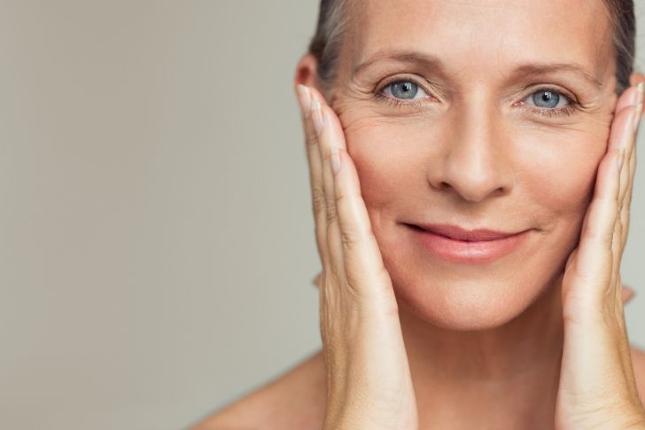 Wrinkle remedies: happy mature woman touching her perfect skin.