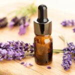 Lavender essential oil in dark bottle with dropper and lavender flowers on wooden surface.