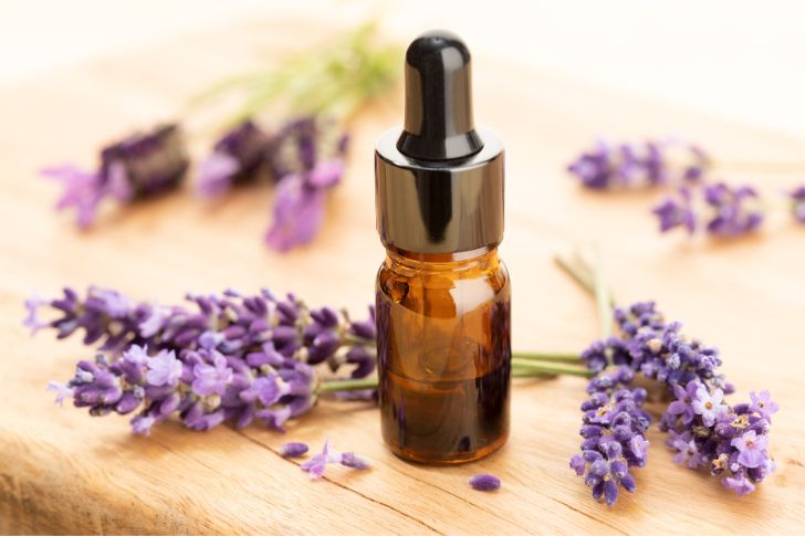 Lavender essential oil in dark bottle with dropper and lavender flowers on wooden surface.