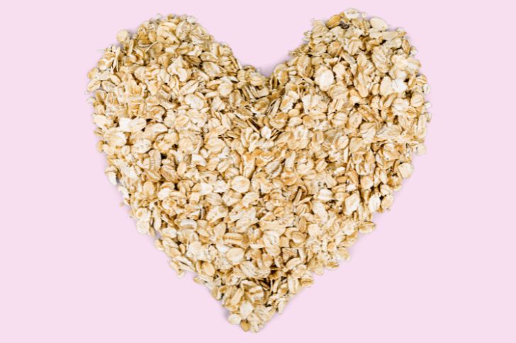 Heap of oat flakes in a shape of heart on pink background, shot from above.